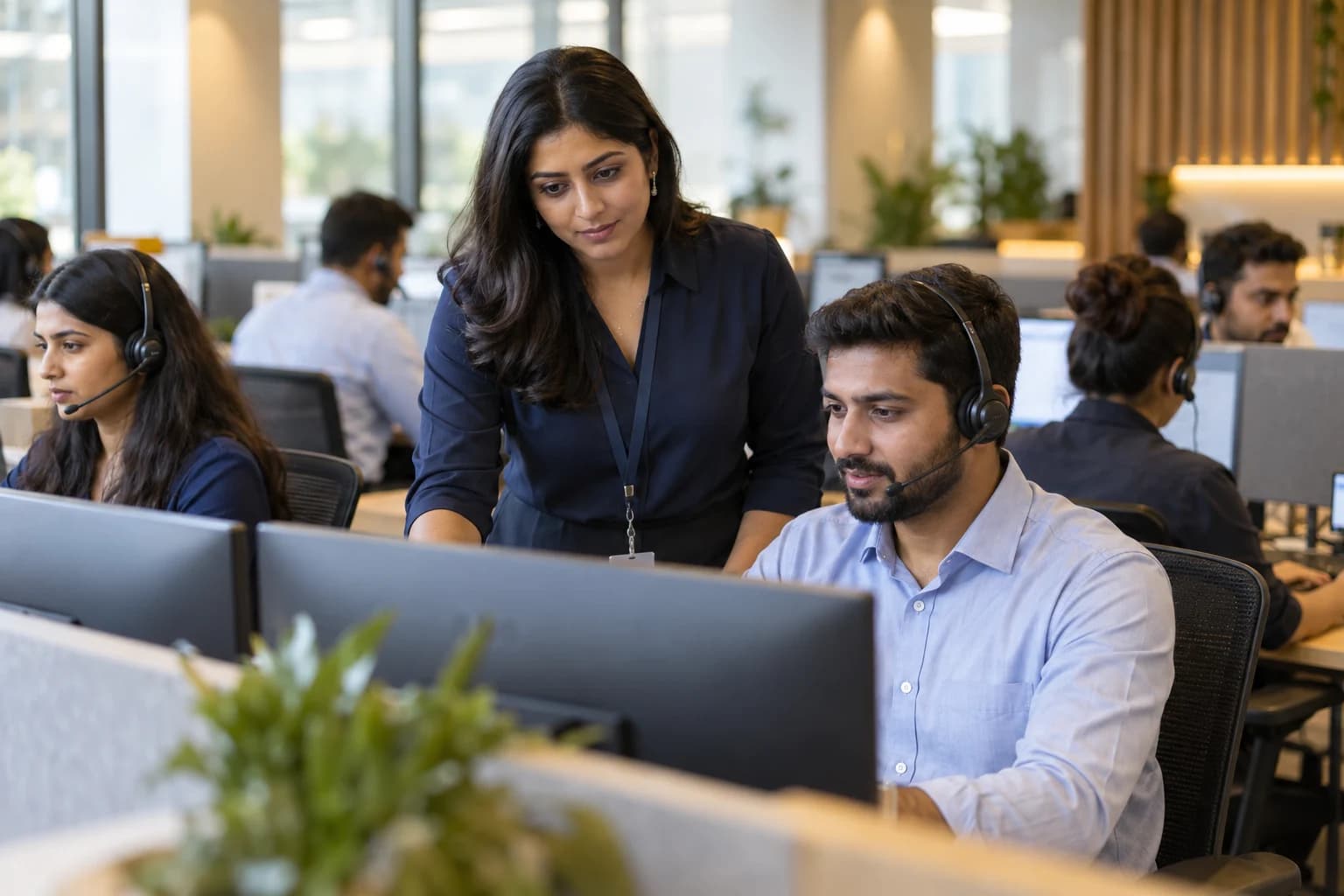 An operations supervisor reviewing work with a headset-wearing support agent on a bright BPO office floor