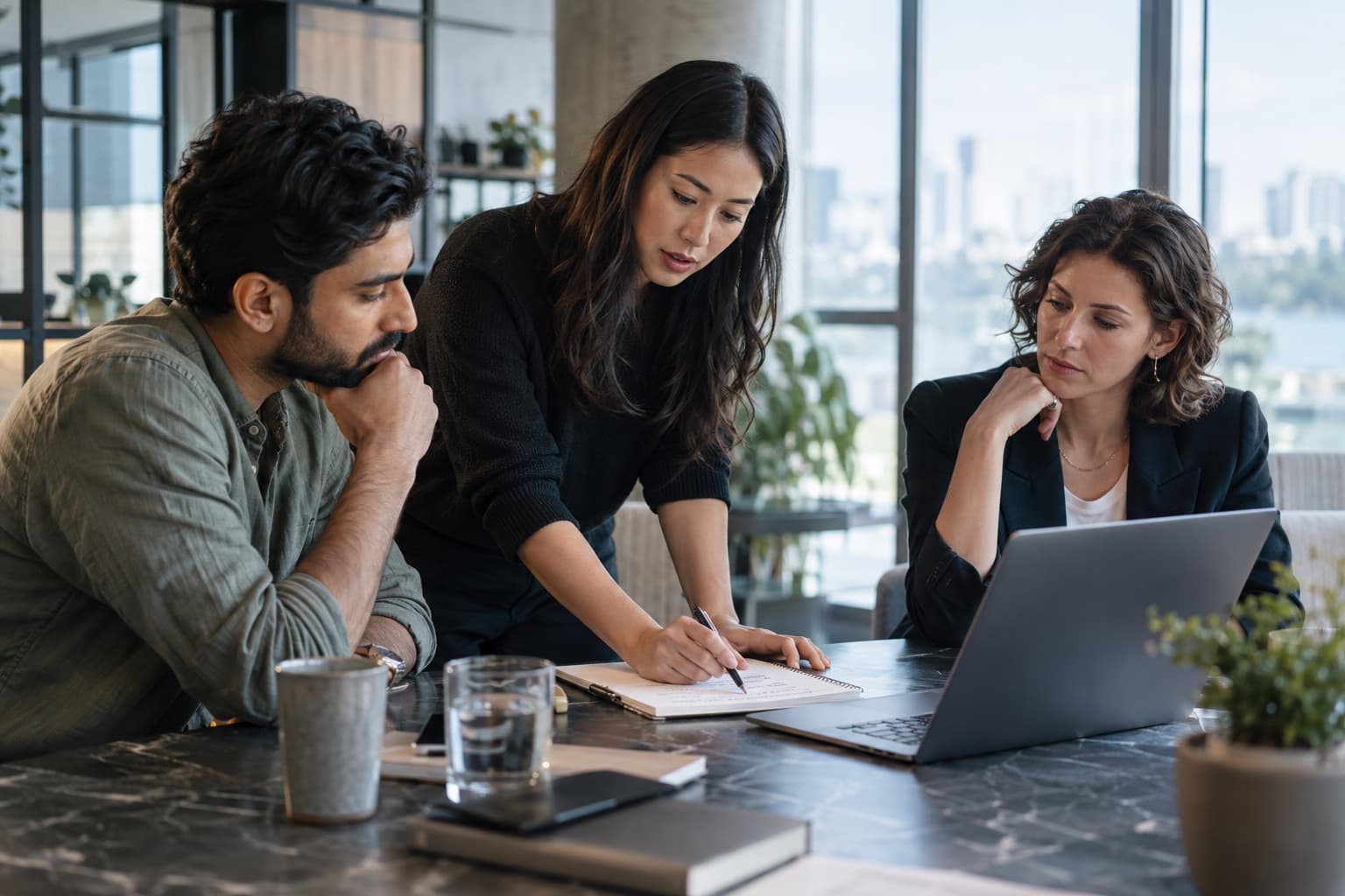 Three colleagues thoughtfully reviewing a work process around a laptop